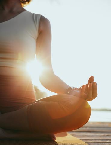 Person meditating in lotus pose at sunrise, silhouette effect