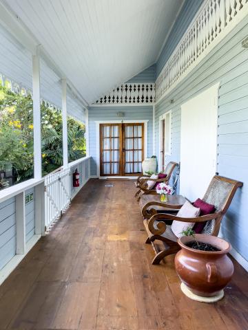 Covered porch with wooden rocking chairs and intricate trim work, surrounded by greenery.