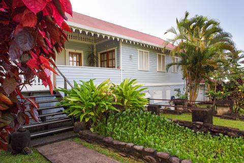 Historical light blue wooden house with red roof in a lush tropical setting