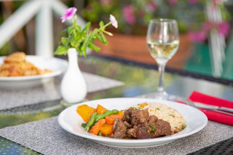 Outdoor dining scene with beef, vegetables, rice, and white wine on a table.