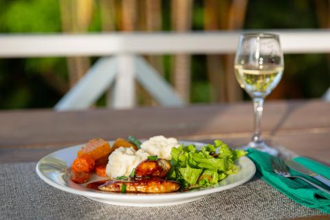 Outdoor meal with salad, mashed potatoes, grilled veggies, sausages, and white wine.