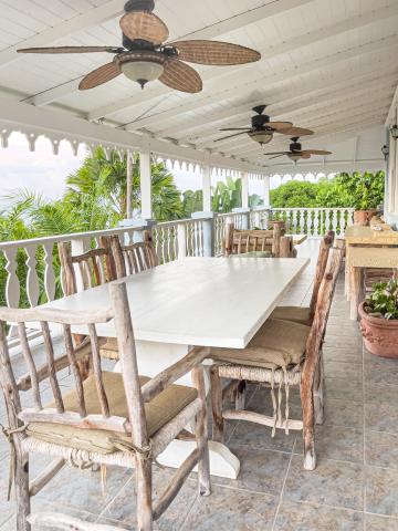Rustic wooden outdoor dining area on porch with lush greenery view and ceiling fans.