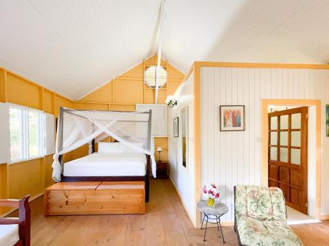 Bright, airy bedroom with white vaulted ceiling and orange wall, elegant four-poster bed.