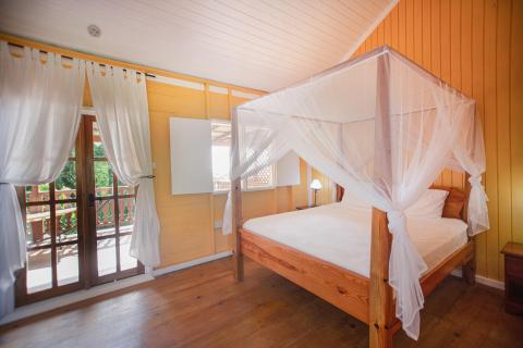 Cozy wooden bedroom with four-poster bed and white mosquito net, leading to a balcony.