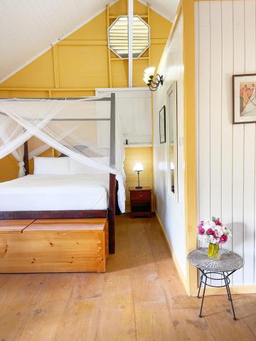Cozy yellow-ceiling bedroom with draped bed, wooden floors, and bright skylight.