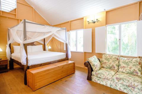 Tropical style bedroom with four-poster bed, wooden details, and lush outdoor views.