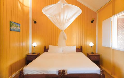 Cozy tropical bedroom with double bed, wooden walls, and soft lighting.