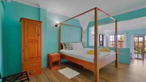 Tropical bedroom with turquoise walls, wooden four-poster bed, and natural light.
