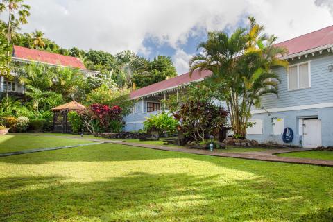 Tropical estate with blue walls, red roofs, surrounded by lush greenery and a gazebo.