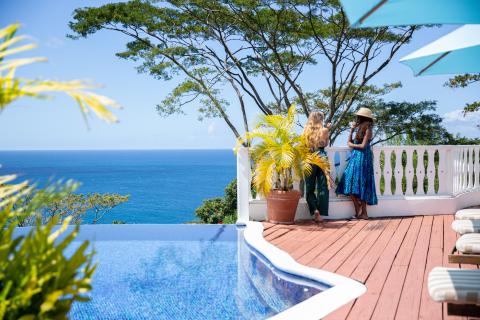 Two women chat on a terrace with infinity pool overlooking the ocean.