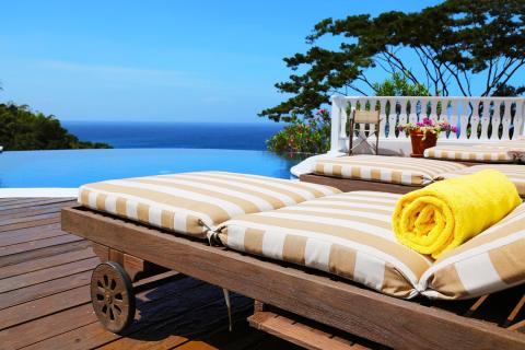 Resort outdoor with sun lounger, infinity pool, ocean view, and lush foliage.