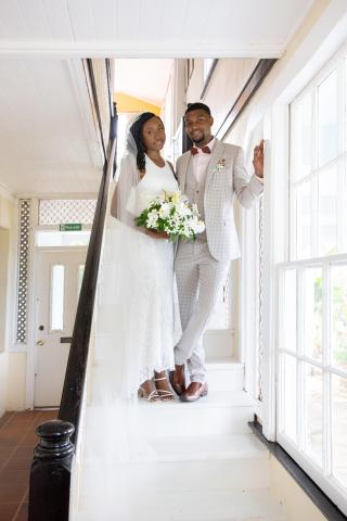 Bride in white dress and groom in gray suit smiling on a staircase