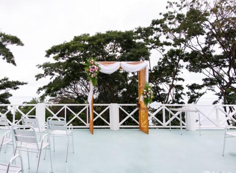 Outdoor wedding venue with floral arch, white chairs, and scenic waterfront backdrop.