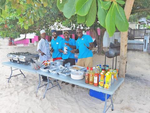 Four men enjoying a beach barbecue with grilling and drinks.