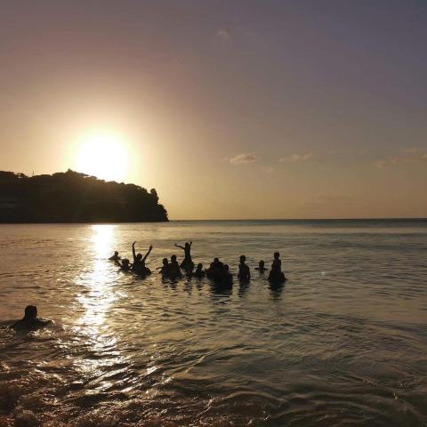 Group enjoying sea at sunset with hill silhouette and sun reflection