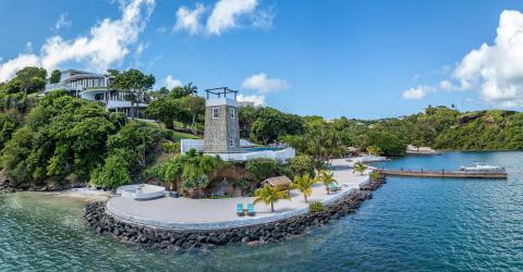 Luxurious coastal villa with a stone tower, sandy beach, and private pier.