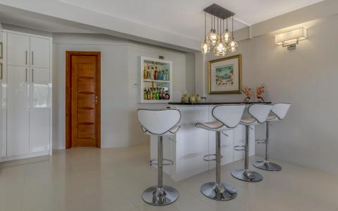 Modern minimalist home bar with white stools and a tropical art piece