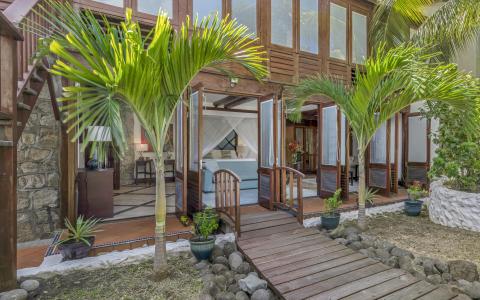 Tropical home entrance with wooden doors, canopy bed, and lush greenery.