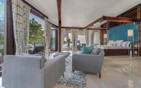 Luxurious bedroom with teal bedding, dark wood beams, and a view of water and greenery.