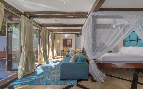 Elegant bedroom with teal bed, blue sofa, wooden beams, and water view.