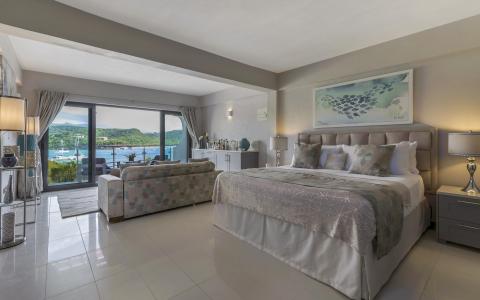 Luxurious bedroom with large bed, floral sofa, and coastal view from balcony.