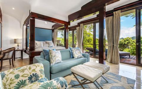 Luxurious bedroom with four-poster bed, blue sofa, and balcony view of greenery.