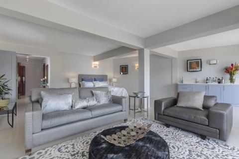 Modern living-bedroom hybrid with grey couches, blue headboard bed, and a small minibar