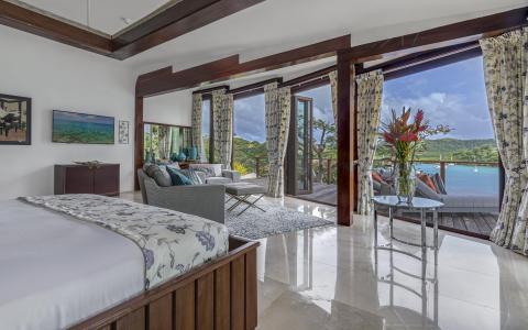 Luxurious room with floral bedding, marble floors, and balcony overlooking water.
