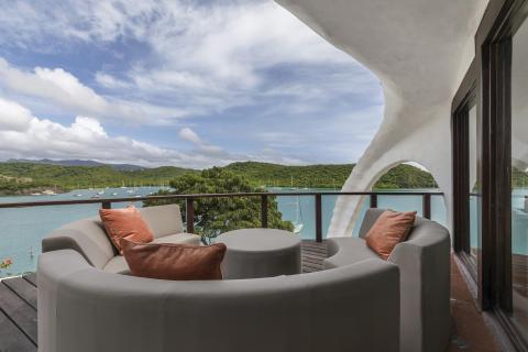 Scenic balcony view with sofa overlooking boats and green coastline, ideal for relaxation.