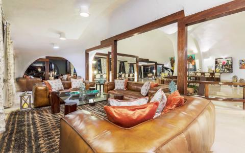Spacious living room with brown leather sofa, glass table, and wooden beams.