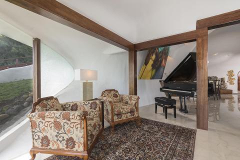 Elegant interior with floral armchairs, grand piano, and large windows overlooking greenery.