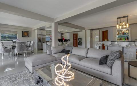 Modern open-plan living room with gray sofa, round dining table, and white kitchen.