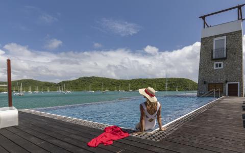 Woman in swimsuit by infinity pool overlooking bay with sailboats