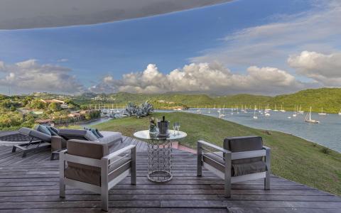 Luxurious outdoor seating area with modern furniture overlooking scenic bay with sailboats.
