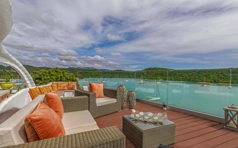 Scenic patio with woven furniture overlooking a vibrant harbor and lush hills.