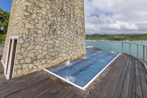 Luxury infinity pool by stone wall overlooking coastal landscape with boats and hills