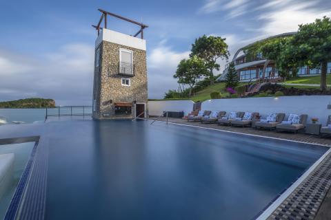 Luxurious poolside with mill-like building and sea view under cloudy skies
