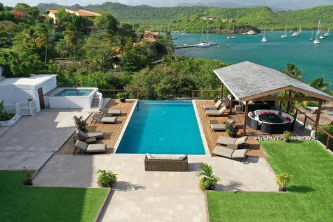Luxurious poolside with hot tub and lounge chairs overlooking a bay with boats.