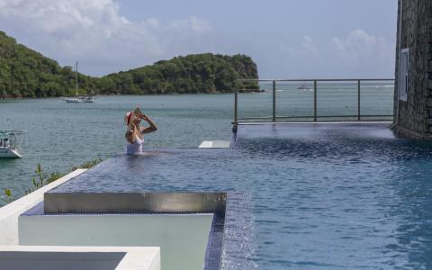 Person in white swimsuit by infinity pool overlooking scenic bay with boats