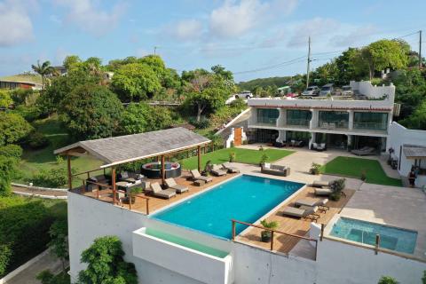 Luxury multilevel villa with rectangular and infinity pools, lush greenery, and modern design.