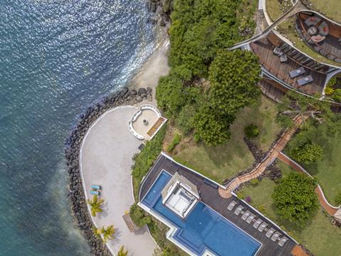 Aerial view of a lush coastal resort with pool and garden.