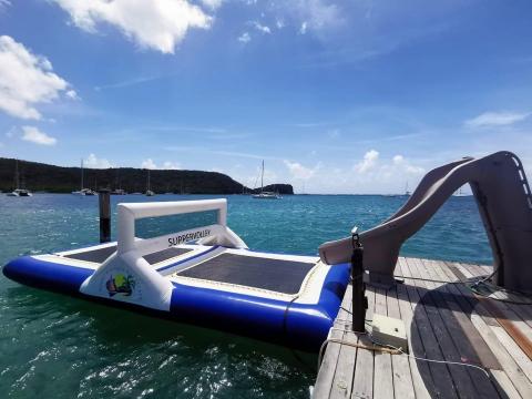 Inflatable water park on clear blue sea with yachts and slide, vacation spot