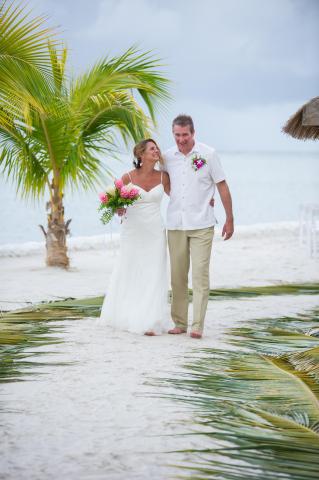 Bride and groom walking on beach under overcast sky, joyful and barefoot.