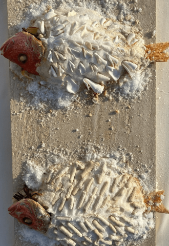 This image displays two fish partially buried in sand, creatively decorated with shells to enhance their textual appearance