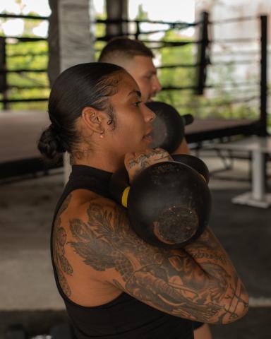 The image shows a woman in a workout setting, lifting a kettlebell