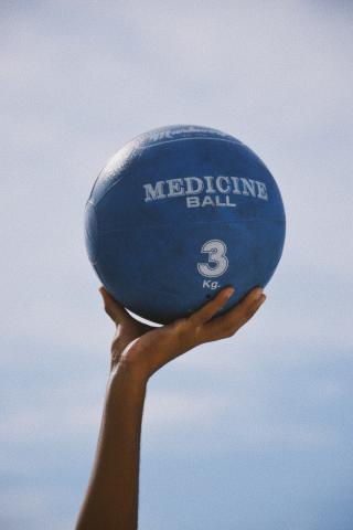 This image features a hand holding up a blue medicine ball against a clear sky background