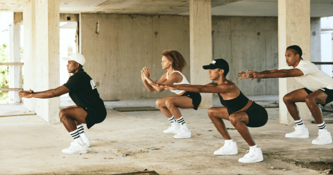 This image shows four individuals performing squats in a synchronized manner in what appears to be an unfinished or abandoned building