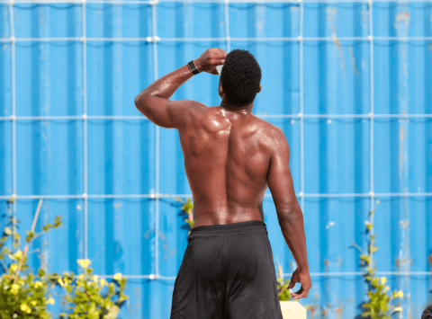 The image shows a man from behind, who appears to be flexing his muscles with his right arm raised, bent at the elbow, gripped by his other hand