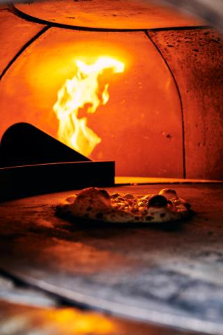 This image shows a pizza cooking inside a wood-fired oven