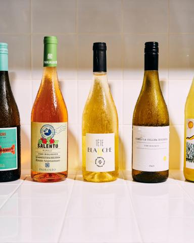 This image features a lineup of five wine bottles placed on a tiled surface, possibly in a kitchen or a bar area